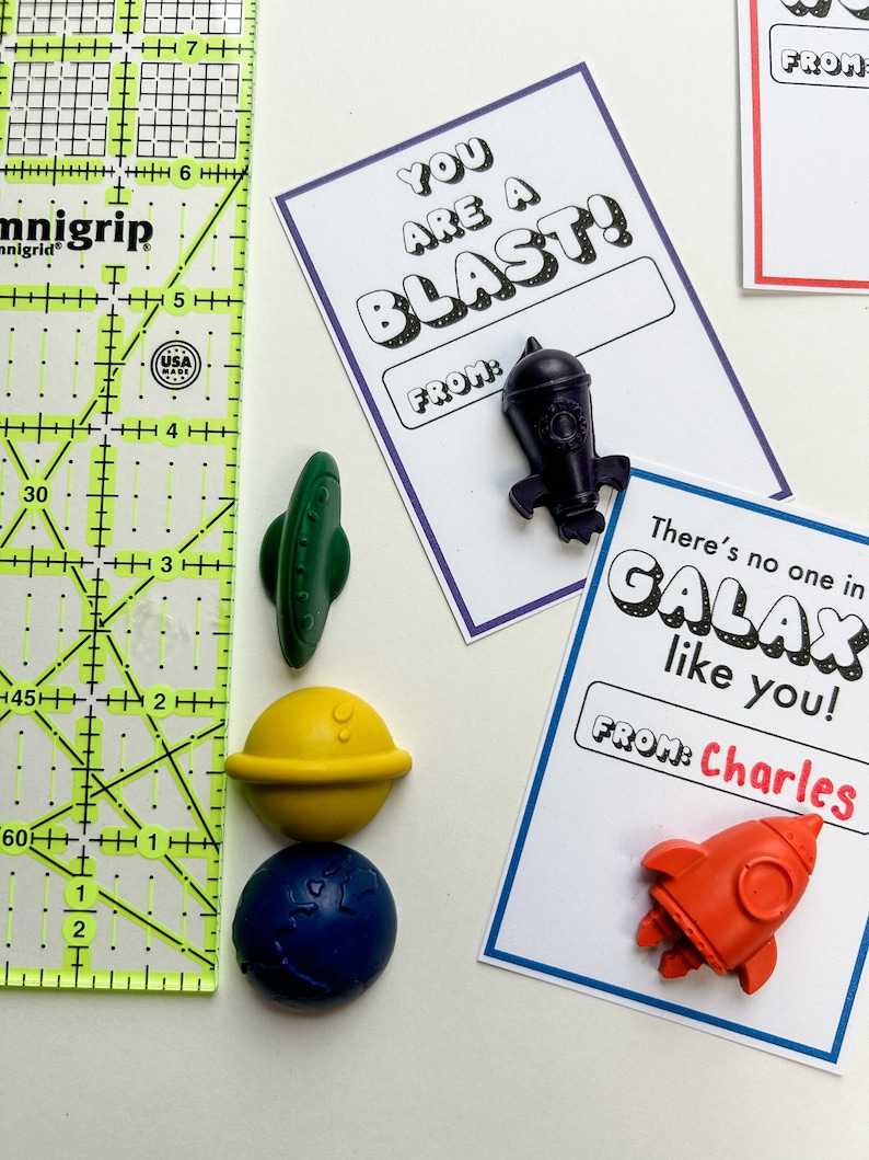 May include: A collection of space-themed Valentine's Day cards and wax crayon shapes. The cards have phrases like "You are a Blast!" and "There's no one in GALAX like you!" with a name field. The crayons are shaped like a rocket, planet, and UFO.