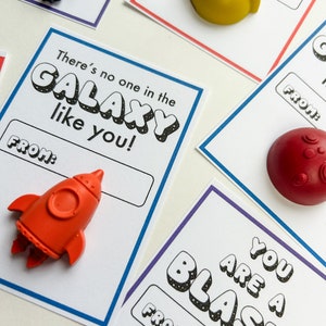 May include: Cards with space-themed designs and accompanying small, colorful plastic shapes. The cards have phrases like "There's no one in the GALAXY like you!" and "YOU ARE A BLAST!" with space-themed shapes like rockets and planets.