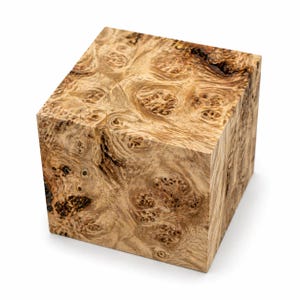 May include: A square wooden block with a unique burl wood grain pattern. The wood features a mix of light and dark brown tones, with intricate swirling and knot-like details. The cube shape is perfect for woodworking or decorative projects.