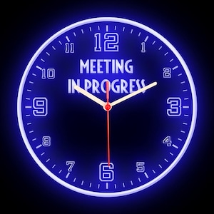 May include: A blue neon clock with the words "MEETING IN PROGRESS" in white. The clock hands are at 1:30. The numbers and the clock's outer ring are also in white, with a blue glow.