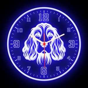 May include: A white clock with a blue background and a white silhouette of a dog's head in the center. The clock face has black numbers and hands. The clock is illuminated with a blue glow.