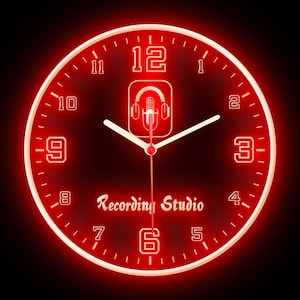 May include: Red illuminated wall clock with white numerals and hands. The clock face features the words "Recording Studio" and a microphone and headphones icon. The clock has a glowing red border and a black background.