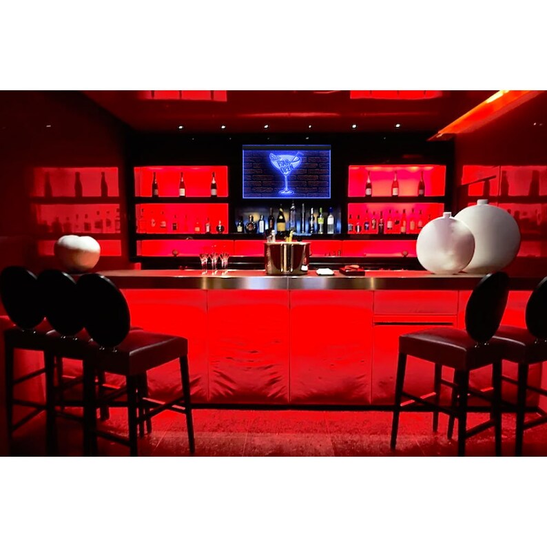May include: A contemporary bar with red lighting and black bar stools. The bar has a stainless steel countertop, shelves with bottles, and a neon cocktail glass sign. White spheres provide contrast.