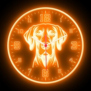 May include: Orange glow clock with a dog silhouette in the center. The clock face has black numbers and hands. The dog is a light brown color.