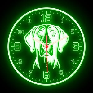 May include: A round, green-glowing wall clock featuring a dog's face in the center. The clock face has white numerals and hands, with a red second hand. The dog's features are outlined in green, creating a striking contrast against the black background.