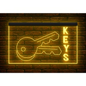 May include: A yellow neon sign with a key outline and the word "KEYS" in block letters. The sign is on a brick wall.