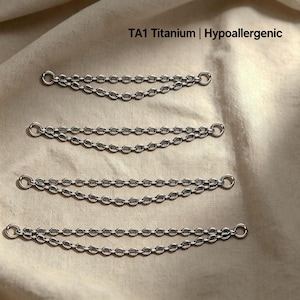 May include: Four silver-toned TA1 titanium double-strand chains of varying lengths, each featuring small circular jump rings at both ends. The text TA1 Titanium | Hypoallergenic is printed in black above the chains.