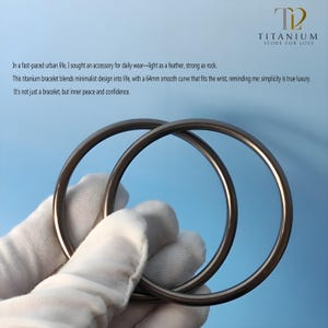 Può includere: Due braccialetti circolari in titanio dal design minimalista e dalla finitura metallica liscia. L'immagine include il testo "TITANIUM STORE FOR LOVE". I braccialetti sono tenuti da una mano guantata. Curva di 6,4 cm.