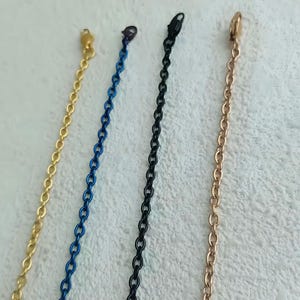 May include: Four chains of different colors: gold, blue, black, and rose gold. The chains are all the same length and have a similar link style.