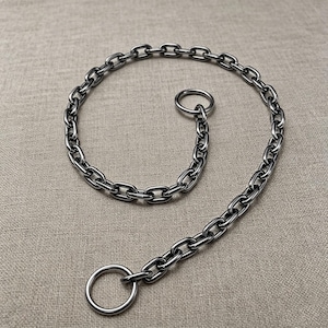 May include: A silver-colored chain collar with a large ring at one end and a smaller ring attached to the chain. The chain is made of interlocking oval links. The collar is designed for a pet.