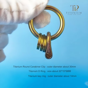 Könnte beinhalten: Ein goldfarbener Titan-Karabinerhaken mit rundem Design, verbunden mit einem Satz Schlüsselringen. Der Text "Titanium Store for Love" ist sichtbar. Der Außendurchmesser des Karabiners beträgt ca. 30 mm.