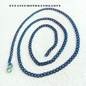 Könnte beinhalten: Eine blaue Titan-Kette mit einem Karabinerverschluss. Die Kette ist im Curb-Stil mit einem leicht schimmernden Finish.