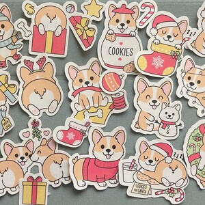 May include: A set of 15 Christmas-themed stickers featuring adorable cartoon corgis in various holiday activities, including holding presents, wearing Santa hats, and decorating a Christmas tree. The stickers are printed on white paper with a glossy finish.