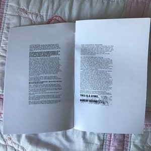 Op de afbeelding: Een open boek met tekst op de pagina's, liggend op een roze en witte quilt. De rechterpagina heeft de tekst "THIS IS A STORY WORTH TELLING" in een zwart kader. De linkerpagina heeft ook tekst.