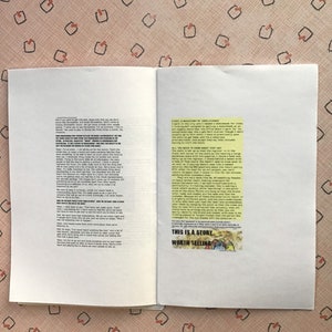 Op de afbeelding: Een open boek met zwarte tekst op de pagina's. Een kleine afbeelding met de tekst "THIS IS A STORY WORTH TELLING" staat op de rechterpagina. De achtergrond is een roze oppervlak met een patroon.