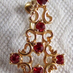 May include: Gold tone earring with a dangling design featuring red rhinestones.