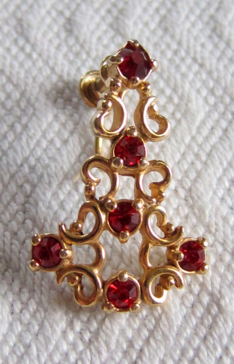 May include: Gold tone earring with a dangling design featuring red rhinestones.