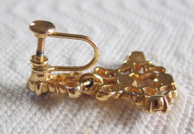 May include: Gold tone clip-on earrings with a floral design. The earrings have a screw-back closure.