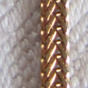 May include: A gold chain necklace with a woven pattern.