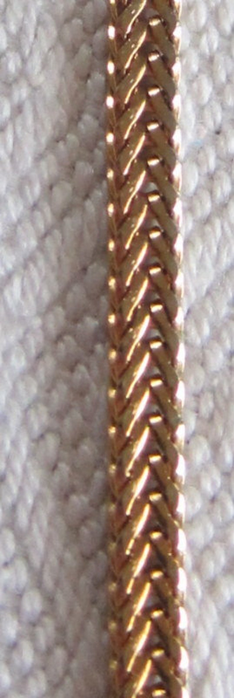 May include: A gold chain necklace with a woven pattern.