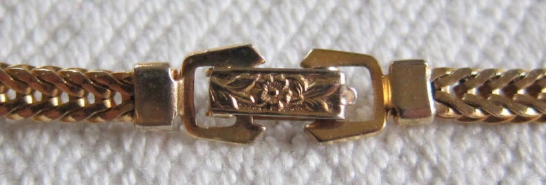 May include: A gold chain bracelet with a detailed floral clasp.