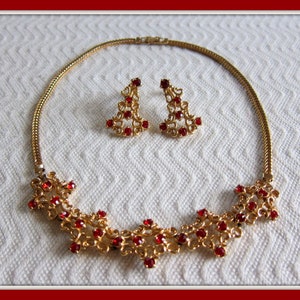 May include: A gold necklace and earrings set with a delicate filigree design and red rhinestone accents.