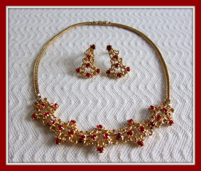 May include: A gold necklace and earrings set with a delicate filigree design and red rhinestone accents.