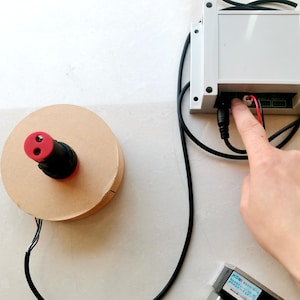 Może przedstawiać: Zbliżenie na czarny przewód elektryczny wpięty do białego pudełka z czerwonym i czarnym kablem. Pudełko ma etykietę z tekstem "KOB - 控制器".