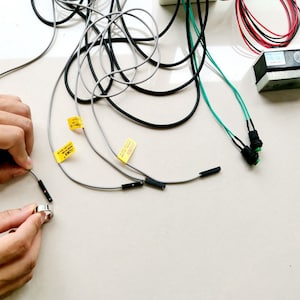 May include: A close-up of a set of electrical components, including a pair of black and green push button switches, a pair of black and gray sensors, and a tangle of grey and black wires.