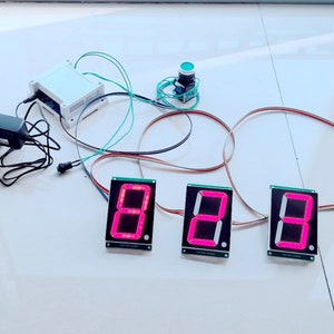 May include: Three red LED digital displays with a black background and white text. The displays show the number 8. The displays are connected to a white box with wires and a green button.