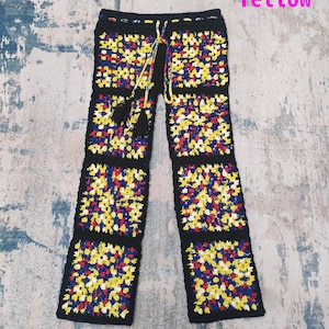 Op de afbeelding: Zwarte gehaakte broek met een kleurrijk geometrisch patroon in geel, rood en blauw. De broek heeft een trekkoord in de taille en een kwastdetail.