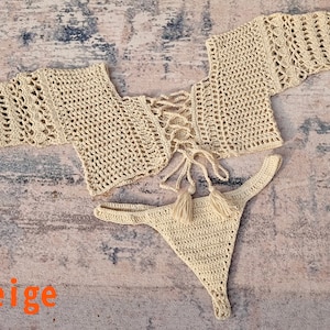 Könnte beinhalten: Beigefarbenes Bikini-Oberteil und -Unterteil aus Häkelarbeit mit Schnürung und Quasten.