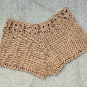 May include: Tan crochet shorts with a scalloped hem and a decorative lace trim around the waistband.