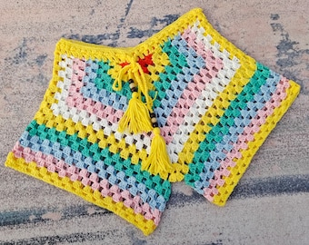 May include: A colorful crocheted garment with a yellow, pink, blue, and green striped pattern. The garment has a yellow tassel and a beaded tie.