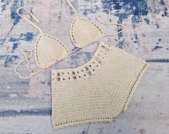 May include: A crocheted bikini set in a cream color. The top is a triangle style with thin straps and the bottom is a high-waisted, short style.