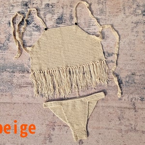 Op de afbeelding: Beige gehaakte tweedelige set. De top is een haltermodel met franjes aan de onderkant. De bijpassende broek is een stringmodel. Het woord "beige" is in het oranje geschreven.