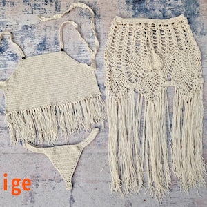 Könnte beinhalten: Beigefarbenes Bikini-Oberteil, -Unterteil und -Rock aus Häkelarbeit mit Fransen. Das Oberteil hat einen Halterneck-Stil und der Rock ist ein Wickelrock.