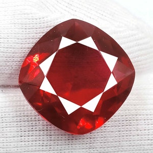 May include: A deep red gemstone with a cushion cut and a starburst pattern. The gemstone is faceted and has a high polish.