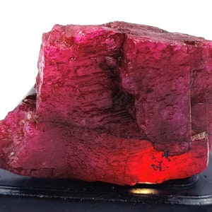 May include: A large, rough, red ruby crystal with a deep, rich color. The crystal has a natural, unpolished appearance and is a beautiful example of this gemstone.