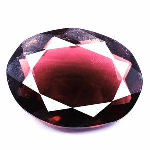 Può includere: Una pietra preziosa ovale di colore rosso intenso con taglio a faccette e un motivo a stella.