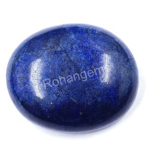 Pode incluir: Uma pedra preciosa de lápis-lazúli polida, de forma oval. A pedra azul escura tem uma superfície lisa e refletora com subtis manchas e veios dourados. A palavra "Rohangem" é visível na superfície.