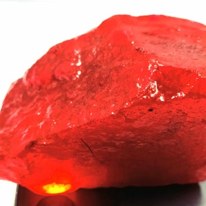 May include: A large, rough, red gemstone with a smooth, polished surface. The gemstone is illuminated from below, casting a warm glow.