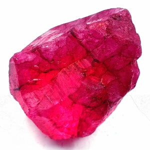 Peut inclure: Un gros cristal de rubis rouge foncé avec une surface brute et facetée. Le cristal a un aspect naturel et non poli.