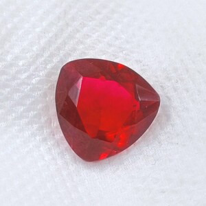 May include: A deep red, faceted gemstone with a triangular shape.