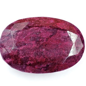 Può includere: Una pietra preziosa ovale di colore rosso scuro con taglio a faccette. La pietra preziosa ha un aspetto leggermente nuvoloso con un tocco di brillantezza.