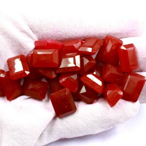 May include: A pile of red gemstone cabochons in a variety of sizes and shapes. The cabochons are smooth and polished, with a glossy finish.