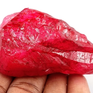 Puede incluir: Una gran gema roja rugosa con un color profundo y rico. La gema tiene un aspecto natural, sin pulir y es probablemente un rubí.