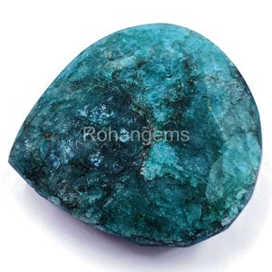Puede incluir: Una piedra preciosa verde azulada con una superficie rugosa y texturizada. La piedra preciosa tiene forma de lágrima y tiene un aspecto natural y orgánico.