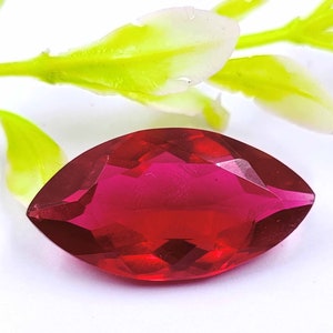May include: A deep red marquise-shaped gemstone with a faceted cut. The gemstone is set against a white background.