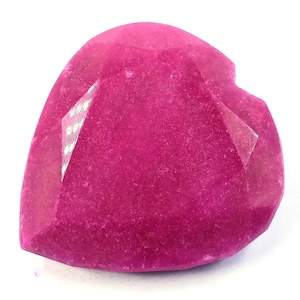 Puede incluir: Una gema facetada en forma de corazón, de un vibrante color magenta. La gema tiene una superficie pulida con múltiples facetas que captan la luz. La gema se encuentra sobre un fondo blanco.